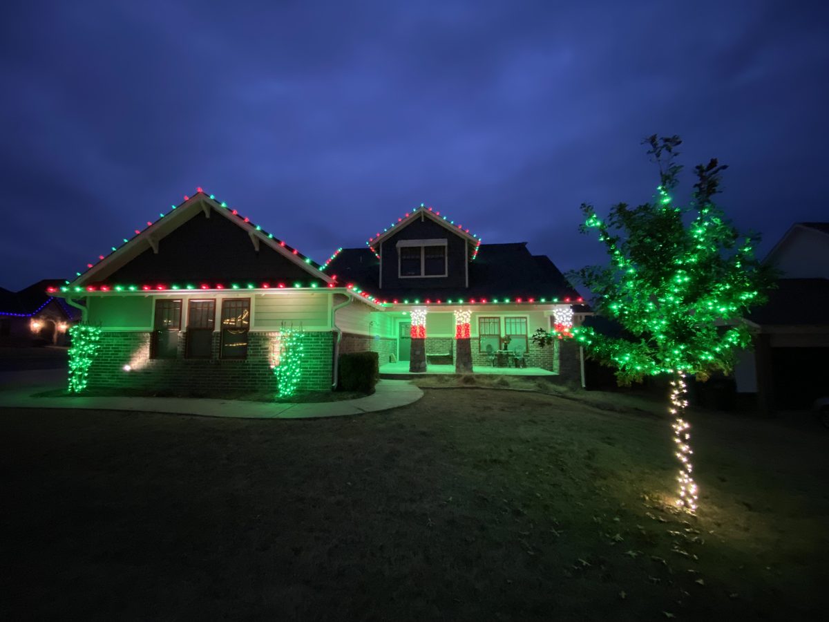 Home with red and green roofline lights and a fully wrapped green tree