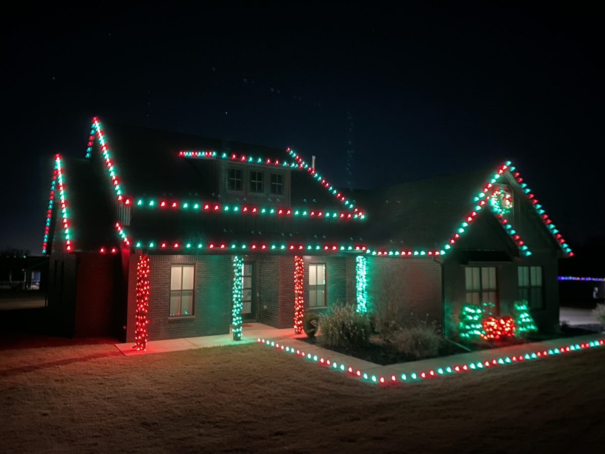 Brick home outlined in red and green lights with wrapped columns and a lit walkway